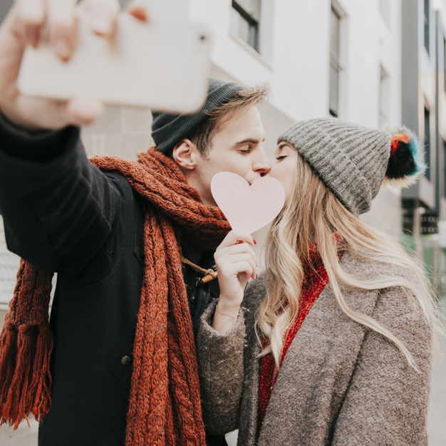 couple-kissing-behind-heart-and-taking-selfie_23-2147736081